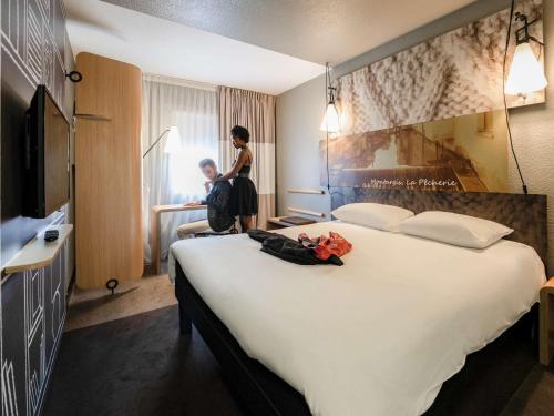 a woman standing next to a large bed in a hotel room at ibis Montargis in Montargis