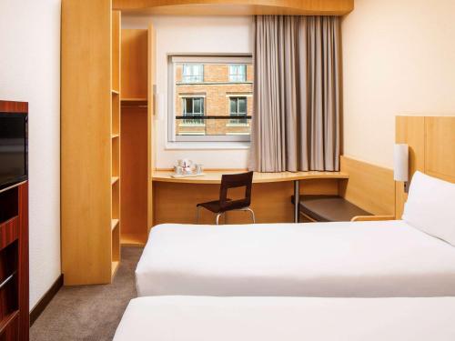 a room with two beds and a desk and a window at ibis Nottingham Centre in Nottingham