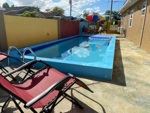 a swimming pool with two chairs and an umbrella at PARADISE VILLA ONSITE PRIVATE POOL ONSITE PRIVATE GYm 2 PROPERTIES SLEEP 12 TO BOOK FOR MORE THAN 6 PLEASE CONTACT US in Ocho Rios