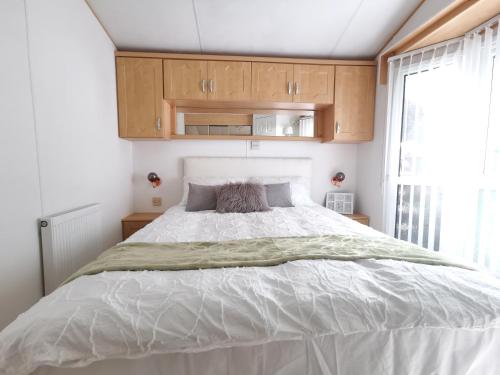 um quarto com uma grande cama branca e armários de madeira em Lakes and woodlands Overstone Holiday Park em Northampton