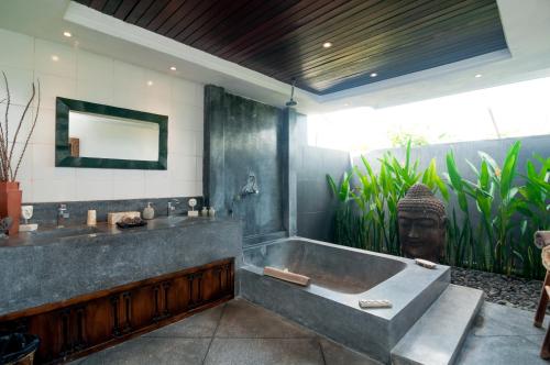 a bathroom with a large tub and a statue of a head at Villa Andaman in Canggu