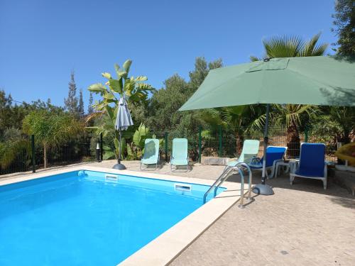a swimming pool with chairs and an umbrella at Monte da Caldeirinha in Luz de Tavira