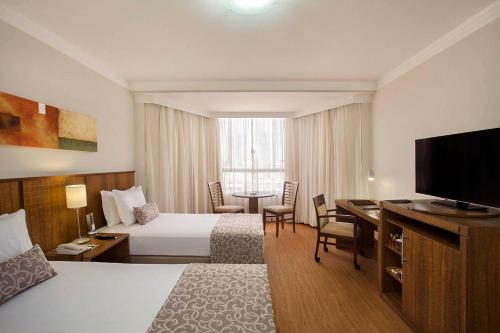 a hotel room with two beds and a table and a television at Windsor Plaza Brasilia in Brasilia
