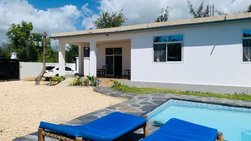 a house with a swimming pool and two blue chairs at Villa Liam B&B Kiwengwa Zanzibar in Kumba Urembo