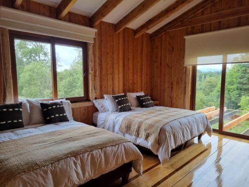two beds in a room with wooden walls and windows at PARCELA DE AGRADO CON PISCINA LAGO RANCO todas las instalaciones con uso exclusivo capacidad 20 personas in Lago Ranco