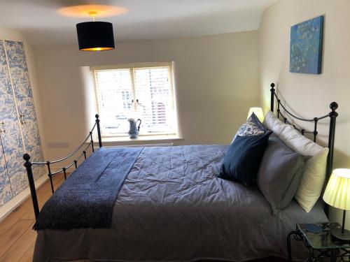 1 dormitorio con cama con sábanas azules y ventana en Church View - c. 1750 cosy character cob cottage., en Hatherleigh