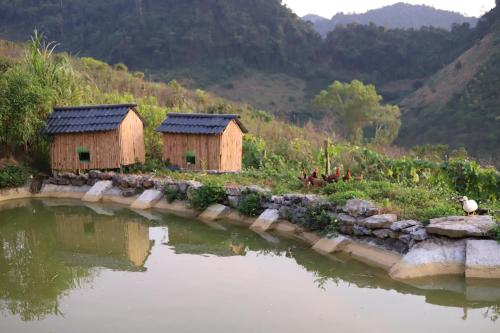 a couple of small huts next to a body of water at Mộc Châu Peachy Garden in An Pon