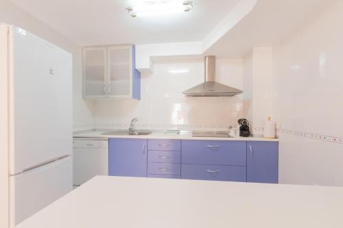 een witte keuken met blauwe kasten en een wastafel bij Agradable casa con piscina in Bolnuevo