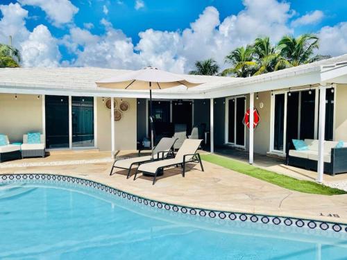 a house with a swimming pool and a patio with chairs and an umbrella at Pompano home with private heated Pool 3D tour available in Pompano Beach