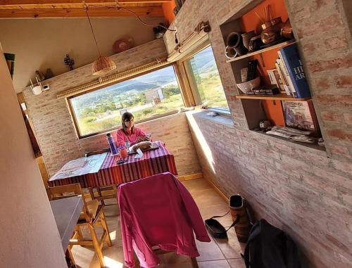 Eine Frau, die an einem Tisch in einem winzigen Haus sitzt. in der Unterkunft La Ribera - Saint Exupéry 90 in El Chalten