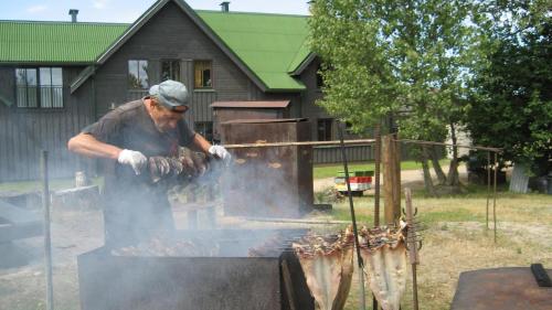 un hombre está cocinando comida en una parrilla en Viesu māja Zvilnis, en Pāvilosta