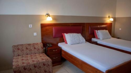 a small room with two beds and a chair at Kunta Kinte Hotel in Accra
