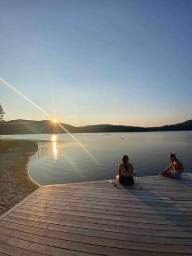 deux personnes assises sur un quai sur une masse d'eau dans l'établissement Fin, enkel leilighet med nydelig strand i nærheten, à Åmdals Verk