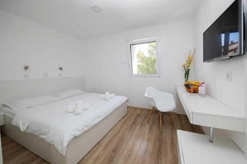 a white room with a bed and a desk and a television at Rooms by the sea Novi Vinodolski - 19837 in Novi Vinodolski