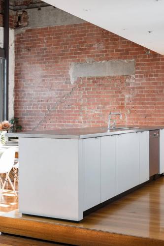 a kitchen with white cabinets and a brick wall at Radiant Richmond Warehouse in Melbourne