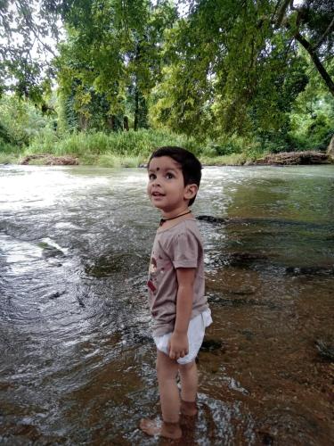 a young boy standing in the water in a river at Jungle Village Homestay in Pinnawala