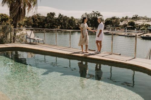 two women standing on a dock next to a swimming pool at Saltwater Villas - Pet Friendly Accommodation in Mooloolaba