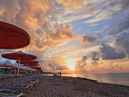 een strand met stoelen en parasols en de zonsondergang bij CASA VACANZE ARBORIAMAR SORSO SARDEGNa in Marina di Sorso