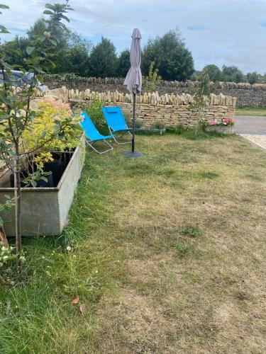 an umbrella and two blue chairs in a garden at Cosy Cotswolds Self-Contained One Bedroom Cottage in Chipping Norton