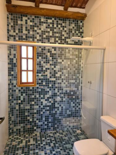 y baño con ducha, aseo y azulejos azules. en Casa Marfim - Privacidade, charme e conforto à 50m do rio, en Caravelas
