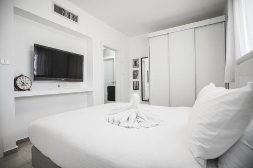 a white bedroom with a bed and a tv at Royal Park By Sun and View in Eilat