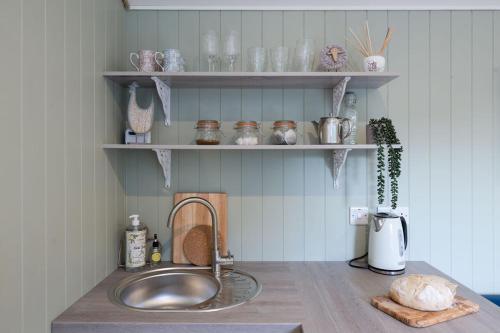 a kitchen counter with a sink and shelves with dishes at Barfield Shepherds Hut in Magherafelt