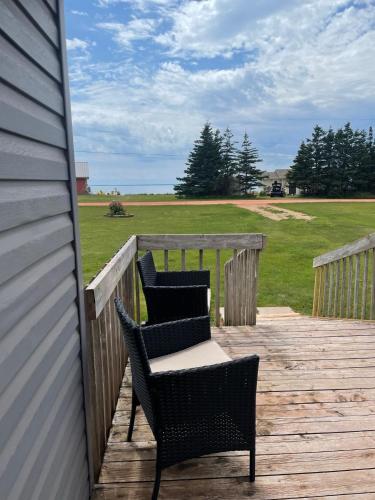 two chairs on a deck with a view of a field at Newly Renovated Confederation Bridge View Cottages in Borden