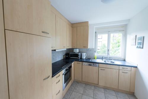 cocina con armarios de madera, fregadero y ventana en Swiss Stay - 2 Bedroom Apartment close to ETH Zurich, en Zúrich