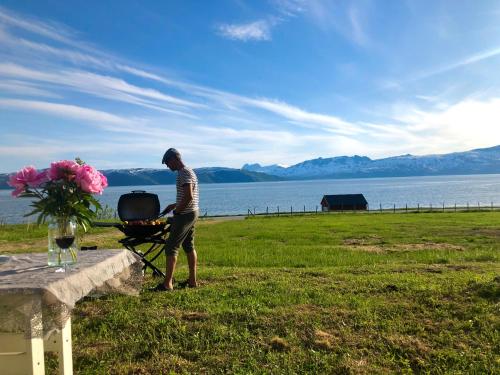 a man standing next to a barbecue grill next to a lake at Unique and charming holiday home with fantastic sea views in Tromsø