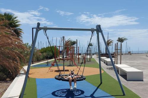 a woman sitting on a swing at a playground at Ocean view apartment in Golf del Sur in San Miguel de Abona