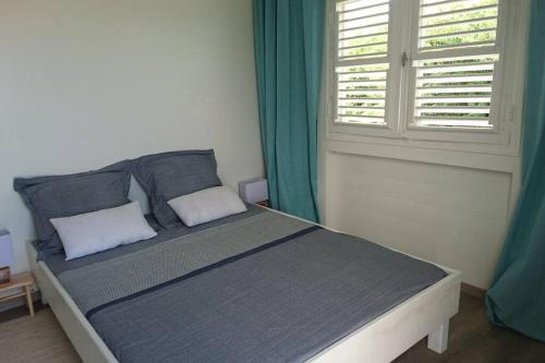 a bedroom with a bed with blue curtains and a window at Héritage créole 1 in Sainte-Luce