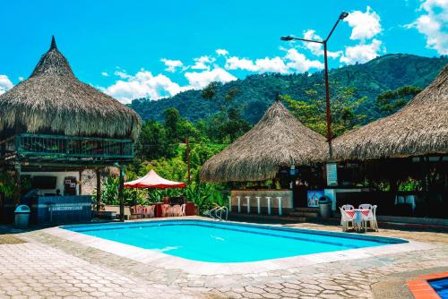 una piscina en un complejo con cabañas de paja en Hotel Hacienda la Bonita, en Amagá