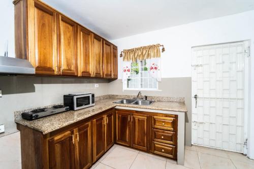cocina con armarios de madera, fregadero y microondas en Skyline Suites 2 Queen bedroom condo en Montego Bay