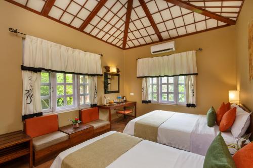 a bedroom with two beds and a desk and windows at Green Mansions Jungle Resort in Sauraha