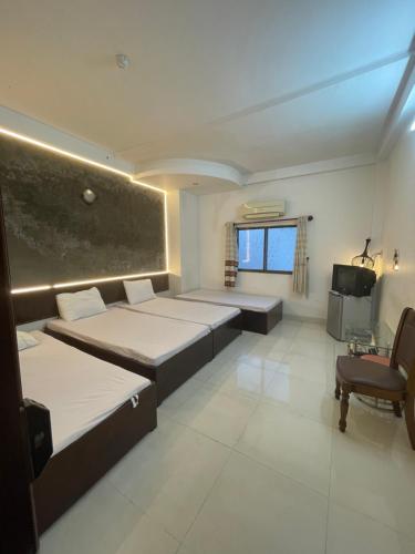 a room with three beds and a chair and a tv at Mai Guest House in Ho Chi Minh City