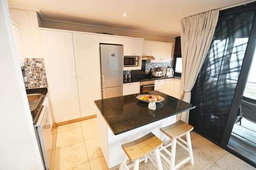 a kitchen with a counter with two chairs and a table at 30 Degrees Beach Apartment Umdloti in Umdloti