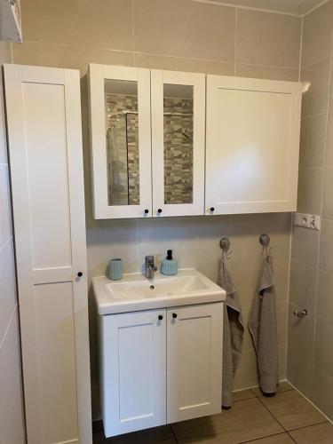 a bathroom with a white sink and white cabinets at Domek nad jeziorem Winiec in Miłomłyn