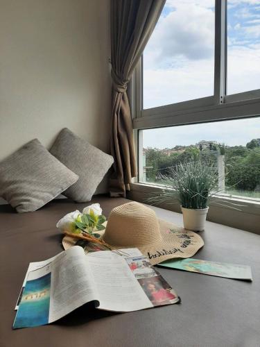 a bed with a book and a hat and a window at Leenova Hotel in Bangkok
