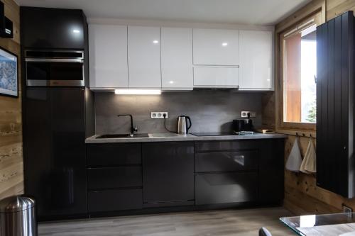 een keuken met witte kasten en een zwarte koelkast bij Courchevel 1550 - SUPERBE appartement SKIS AUX PIEDS ! in Courchevel