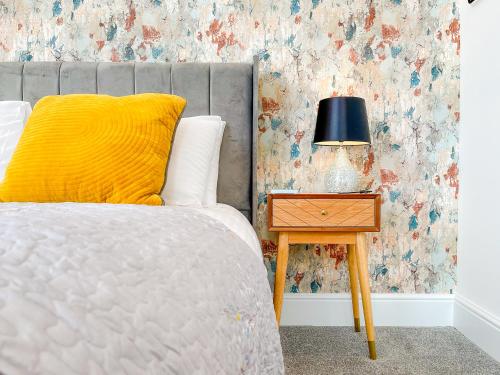 a bed with a yellow pillow and a table with a lamp at Ashfield Boutique Stays in Altrincham