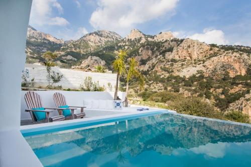 una piscina con sillas y montañas en el fondo en Vento Isolano suites, en Karpathos