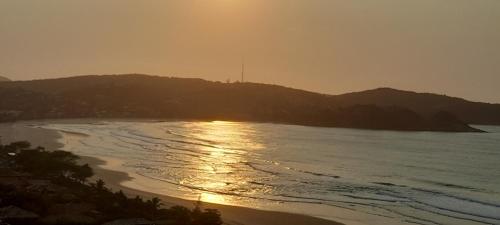 a sunset over the ocean with a hill in the background at 3Suítes, piscina e vista do mar em condomínio pé na areia - pátio compartilhado in Búzios