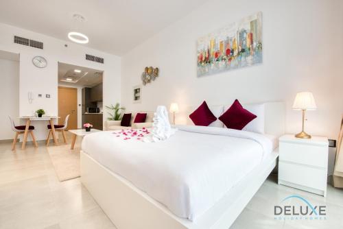 a white bedroom with a large white bed with red pillows at Lovely Studio in Pantheon Elysee JVC by Deluxe Holiday Homes in Dubai