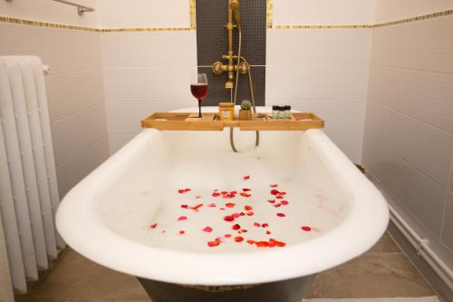 a bath tub filled with red petals and a glass of wine at Joseph Hayn Apartments in Sighişoara