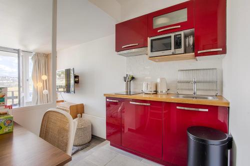 - une cuisine rouge avec évier et four micro-ondes dans l'établissement LA REV'RIE - vue sur mer avec balcon, à Deauville