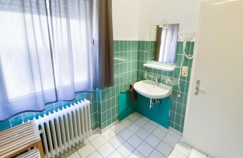 a green tiled bathroom with a sink and a radiator at Hotel garni Bad Café Bad Niedernau in Bad Niedernau