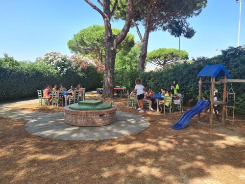 a group of people sitting at tables and a playground at Hotel La Buca Del Gatto in Marina di Cecina