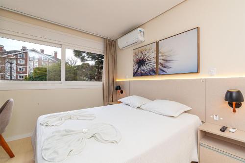 a bedroom with a white bed and a window at 1 quadra da Catedral e 2 vagas de garagem in Canela