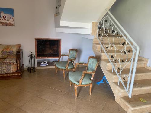 a living room with two chairs and a staircase at Villa avec Piscine, Terrain de Foot et Aire de Jeux pour Enfants in Bir Jedíd Saint-Hubert