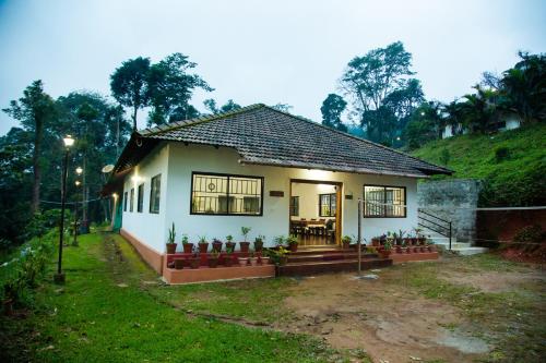 a small white house with a green hill behind it at The Nest bettathur, Coorg in Madikeri